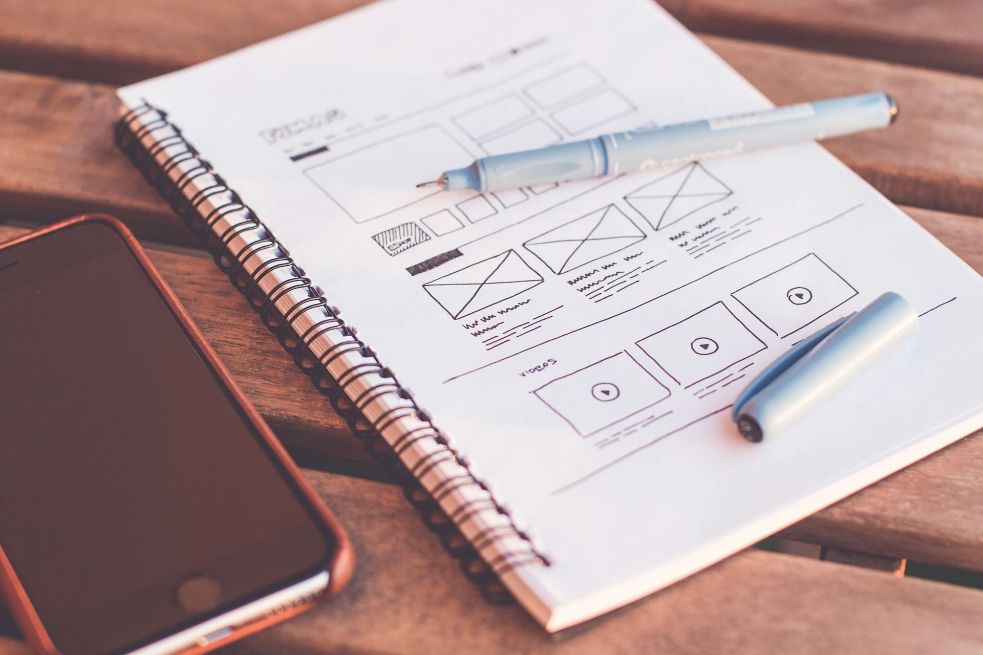 From Syllabus to Sales Page: Write Copy That Converts image Hand-drawn website wireframe in notebook beside phone, planning sales page copy